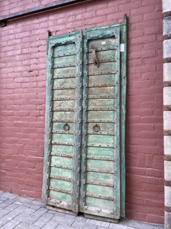 Antique double doors with weathered green paint and metal details, leaning against a red brick wall, vooraanzicht.