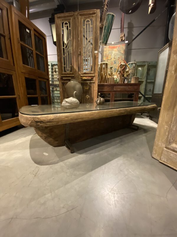 Vintage teakwood boat table with glass top, surrounded by antique wooden furniture, zijaanzicht.